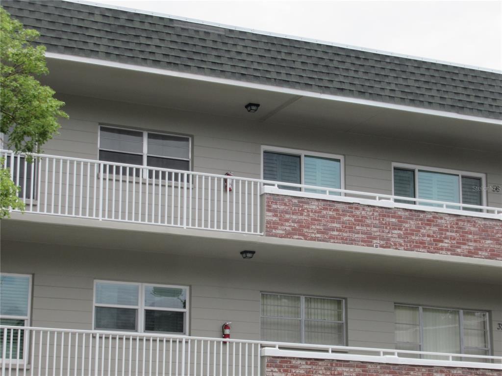 Exterior view of a multi-story apartment building with balconies, brick accents, and sliding windows — 2426 PERSIAN DRIVE UNIT 56, CLEARWATER, FL