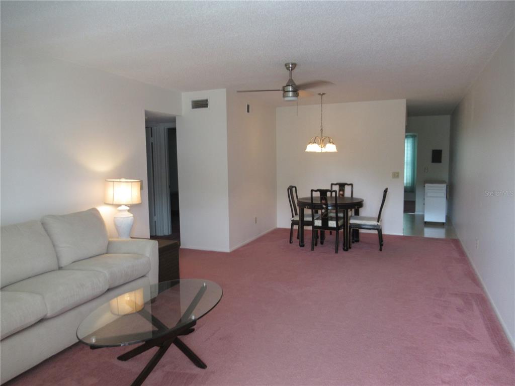 A living and dining area with pink carpeting, a beige sofa, and a glass coffee table — 2426 PERSIAN DRIVE UNIT 56, CLEARWATER, FL
