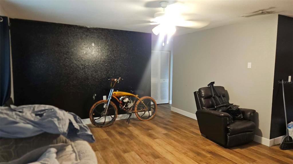 A living room features a black accent wall, wood-look flooring, a ceiling fan, and a bicycle — 18218 DRIGGERS AVENUE, PORT CHARLOTTE, FL