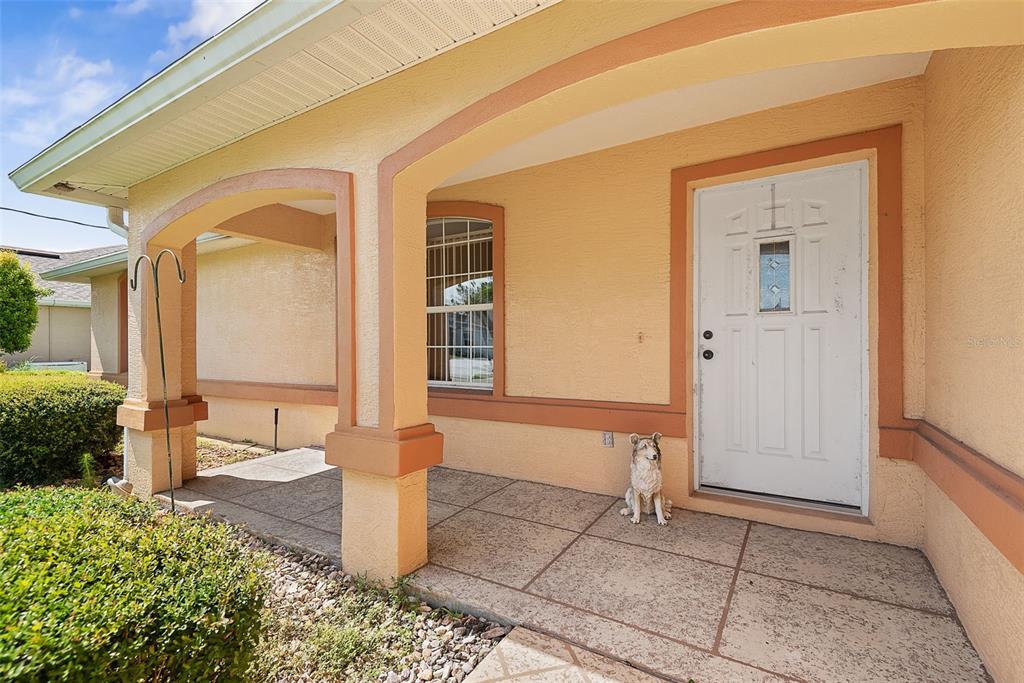 A covered front porch with a white door, a window, and a decorative dog statue — 52 FENWICK LANE, PALM COAST, FL