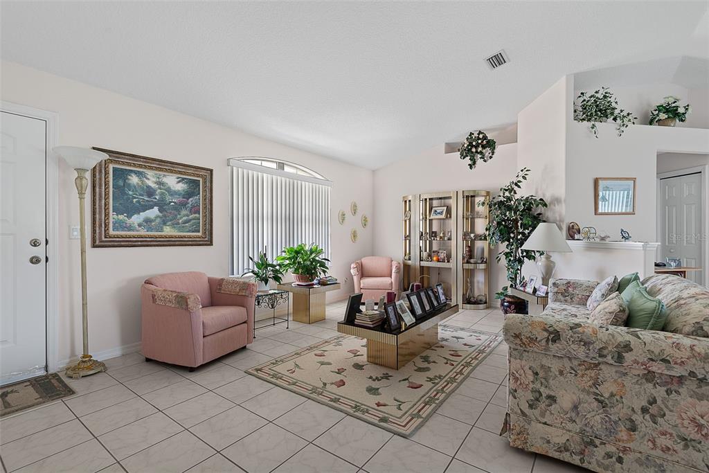 A living room with tile floors, a floral sofa, pink armchairs, and a glass display cabinet — 52 FENWICK LANE, PALM COAST, FL