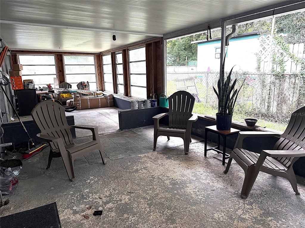 A covered, screened-in concrete patio features three brown plastic chairs and a potted plant — 39246 LIZABETH CIRCLE, ZEPHYRHILLS, FL