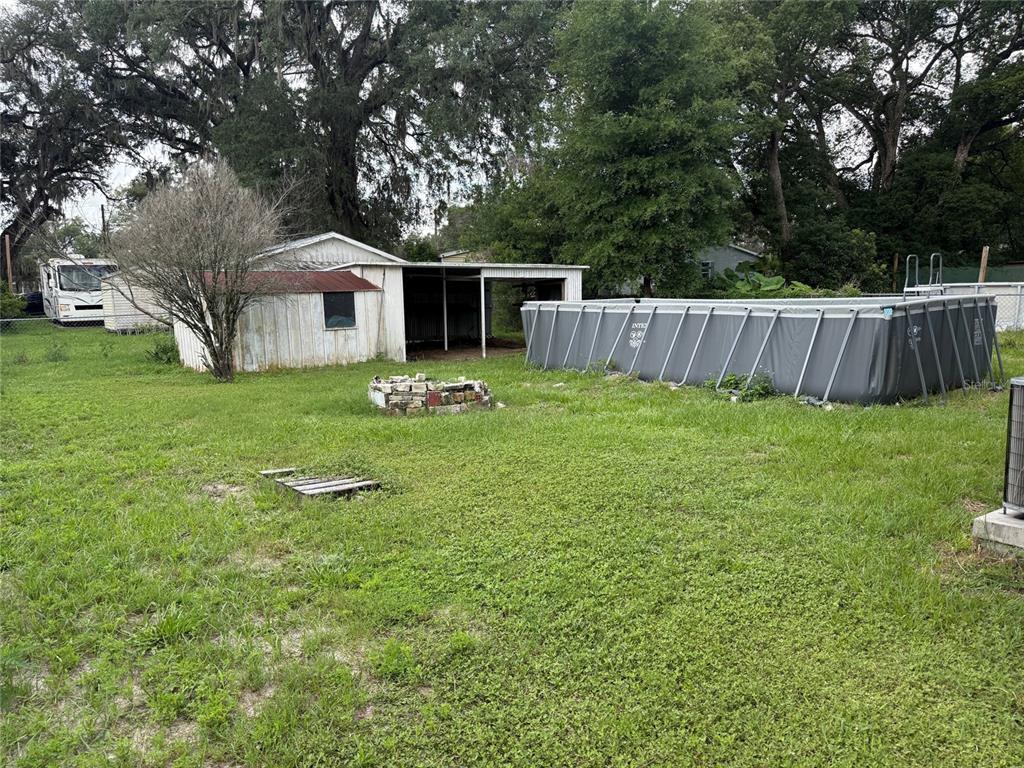 A backyard features a metal shed, an above-ground pool, and a stone fire pit — 39246 LIZABETH CIRCLE, ZEPHYRHILLS, FL