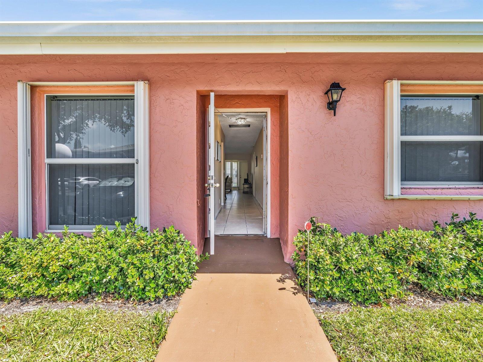 The exterior of a pink stucco house features a front door opening to a hallway — 1610 NW 18th Avenue # 96d, Delray Beach FL 33445, DELRAY BEACH, FL