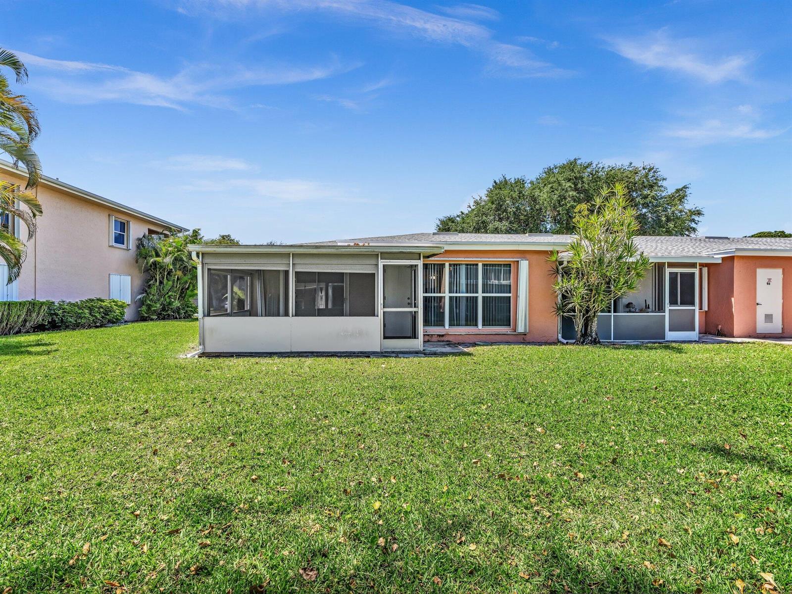 The exterior of a peach-colored house features a screened-in porch and a large grassy yard — 1610 NW 18th Avenue # 96d, Delray Beach FL 33445, DELRAY BEACH, FL