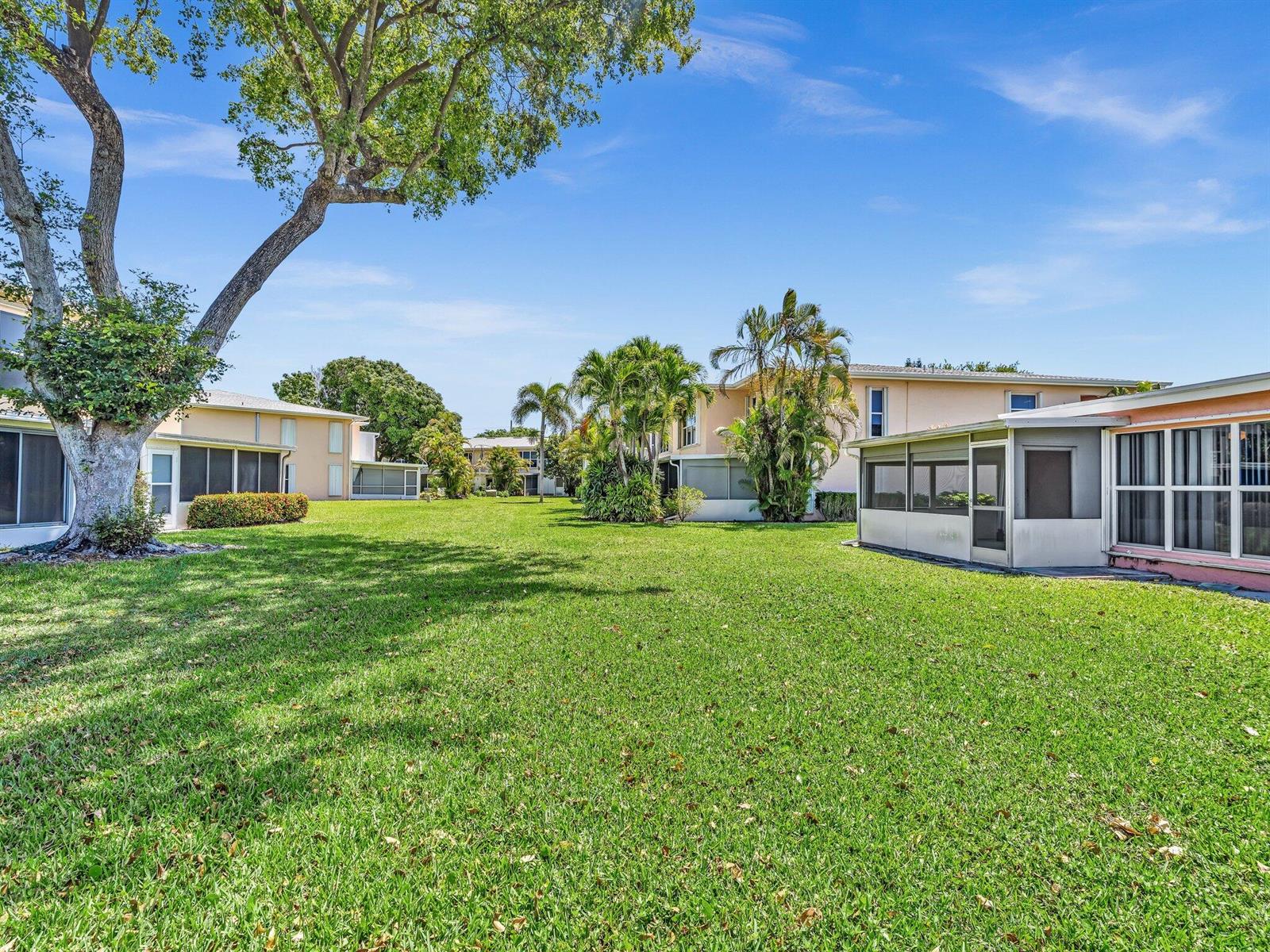 A grassy courtyard sits between multi-story residential buildings with screened-in patios and palm trees — 1610 NW 18th Avenue # 96d, Delray Beach FL 33445, DELRAY BEACH, FL