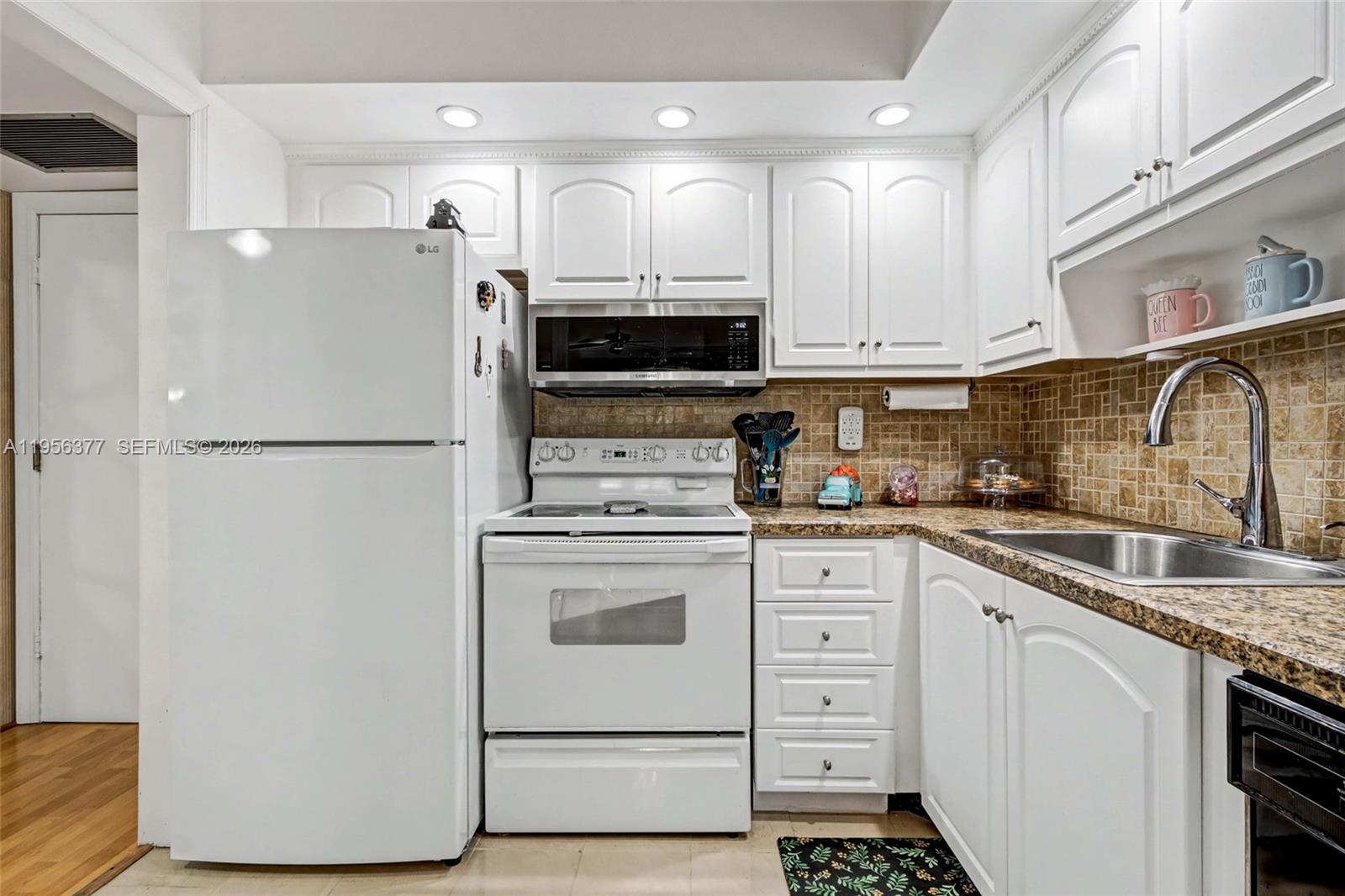 A kitchen features white cabinets, a white refrigerator, a white stove, and a tiled backsplash — 5661 SW 2nd Ct # 101, Margate FL 33068, MARGATE, FL