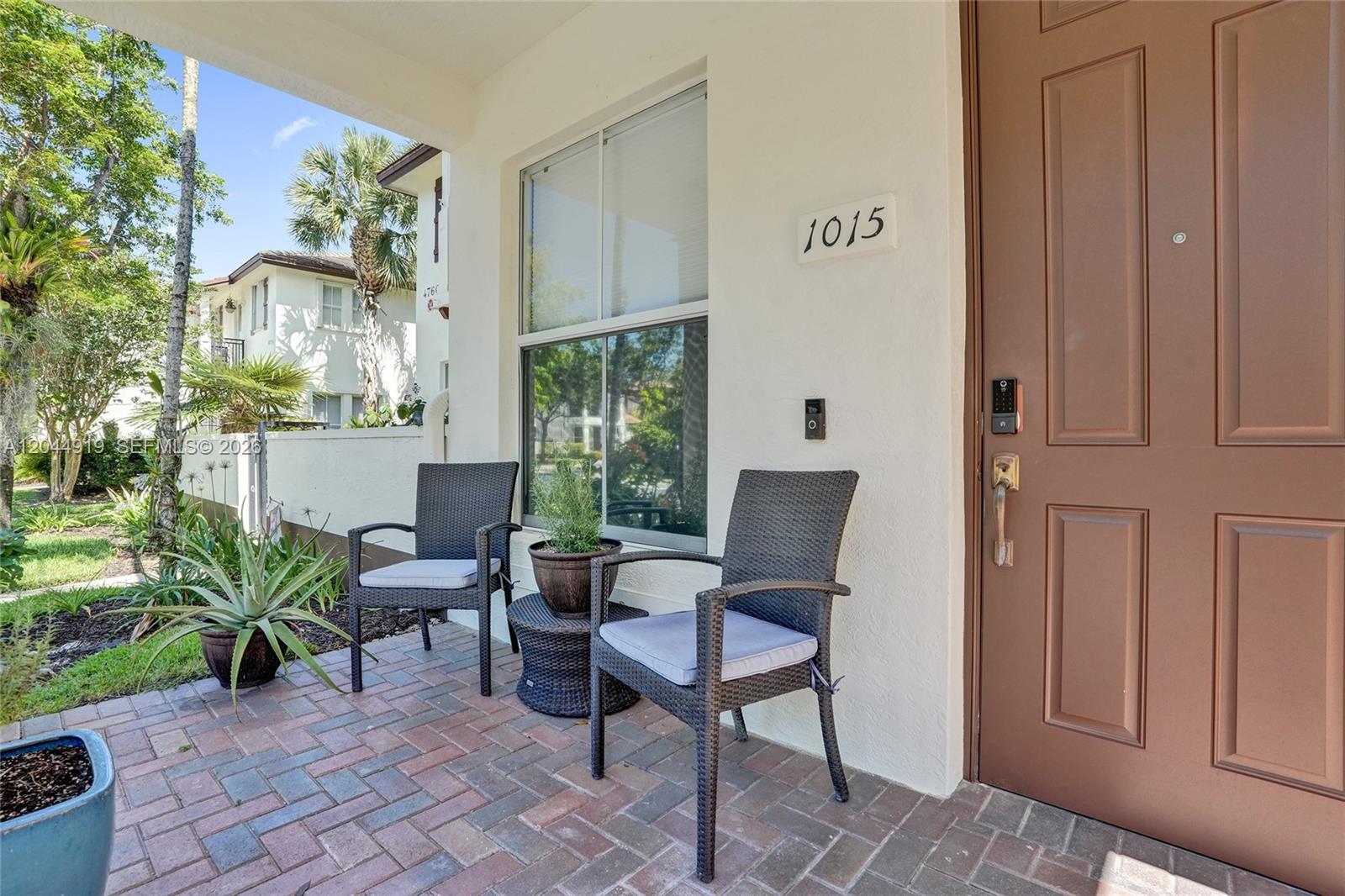 A paved front porch features two wicker chairs, a small table, and a brown door — 4760 Mimosa Pl # 1015, Coconut Creek FL 33073, COCONUT CREEK, FL