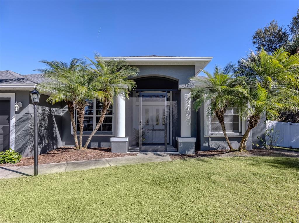 A gray single-story house features a covered entryway with white columns and two palm trees — 5242 ABDELLA LANE, NORTH PORT, FL