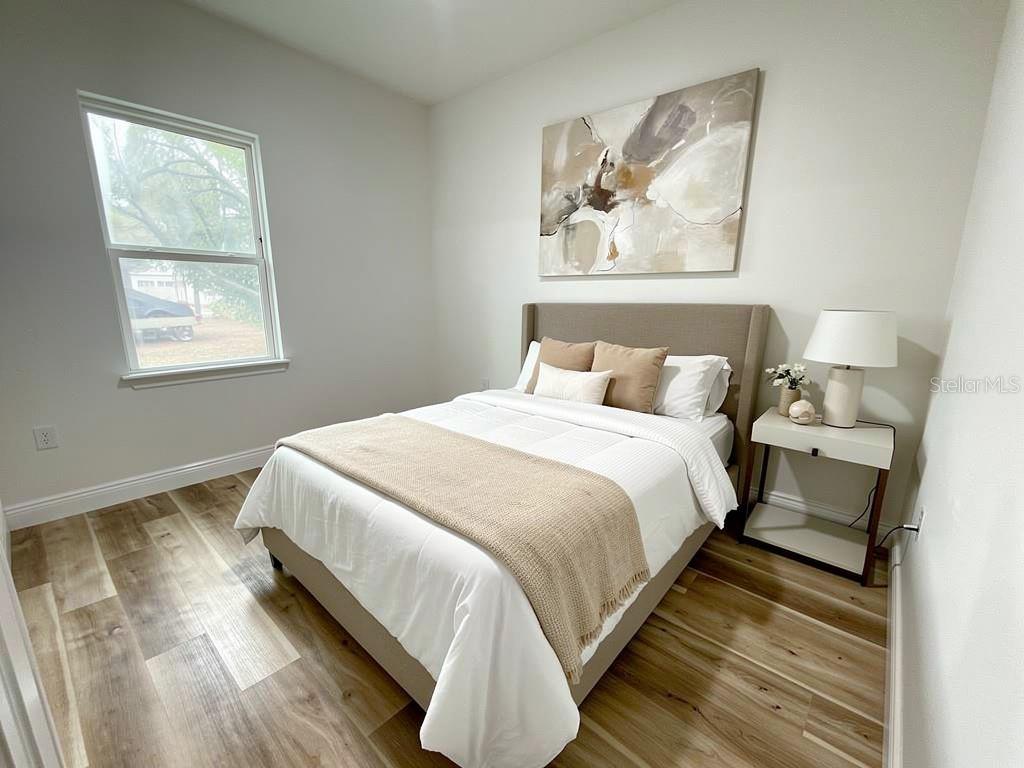 A bedroom features a bed with neutral bedding, a headboard, and wood-look flooring — 23419 GEMSTONE AVENUE, PORT CHARLOTTE, FL