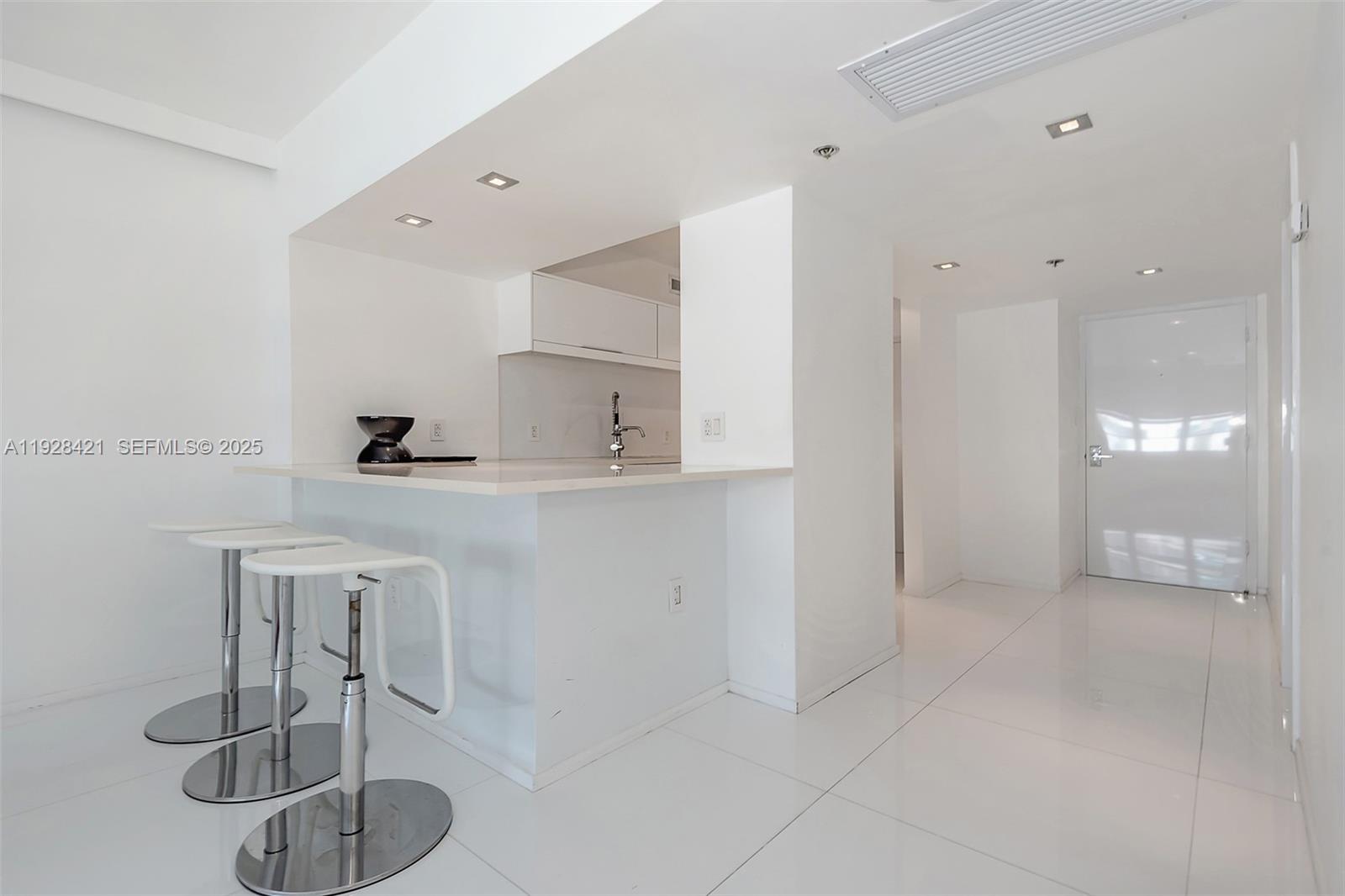 A modern white kitchen features a breakfast bar with three stools and glossy tile floors — 100 Lincoln Rd # 839, Miami Beach FL 33139, MIAMI BEACH, FL