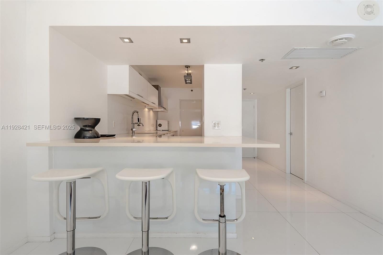 A modern kitchen features white cabinetry, a breakfast bar with three stools, and tiled floors — 100 Lincoln Rd # 839, Miami Beach FL 33139, MIAMI BEACH, FL