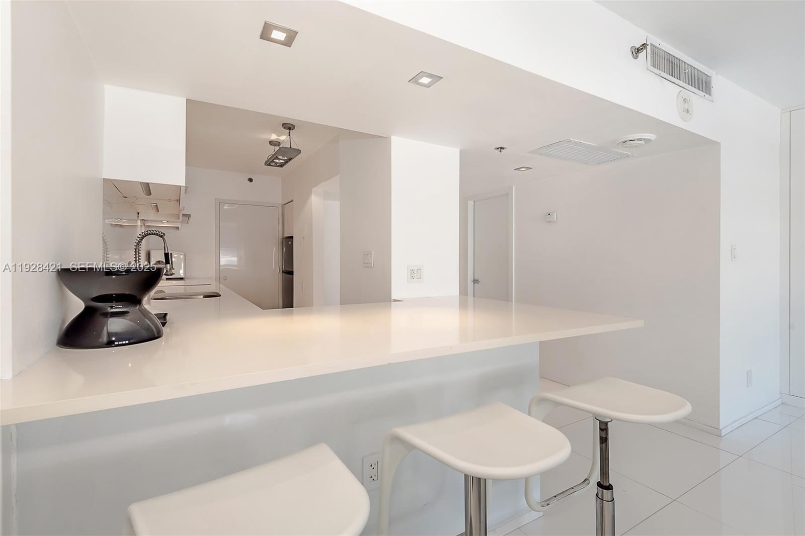 A white kitchen features a breakfast bar with three stools and recessed ceiling lighting — 100 Lincoln Rd # 839, Miami Beach FL 33139, MIAMI BEACH, FL