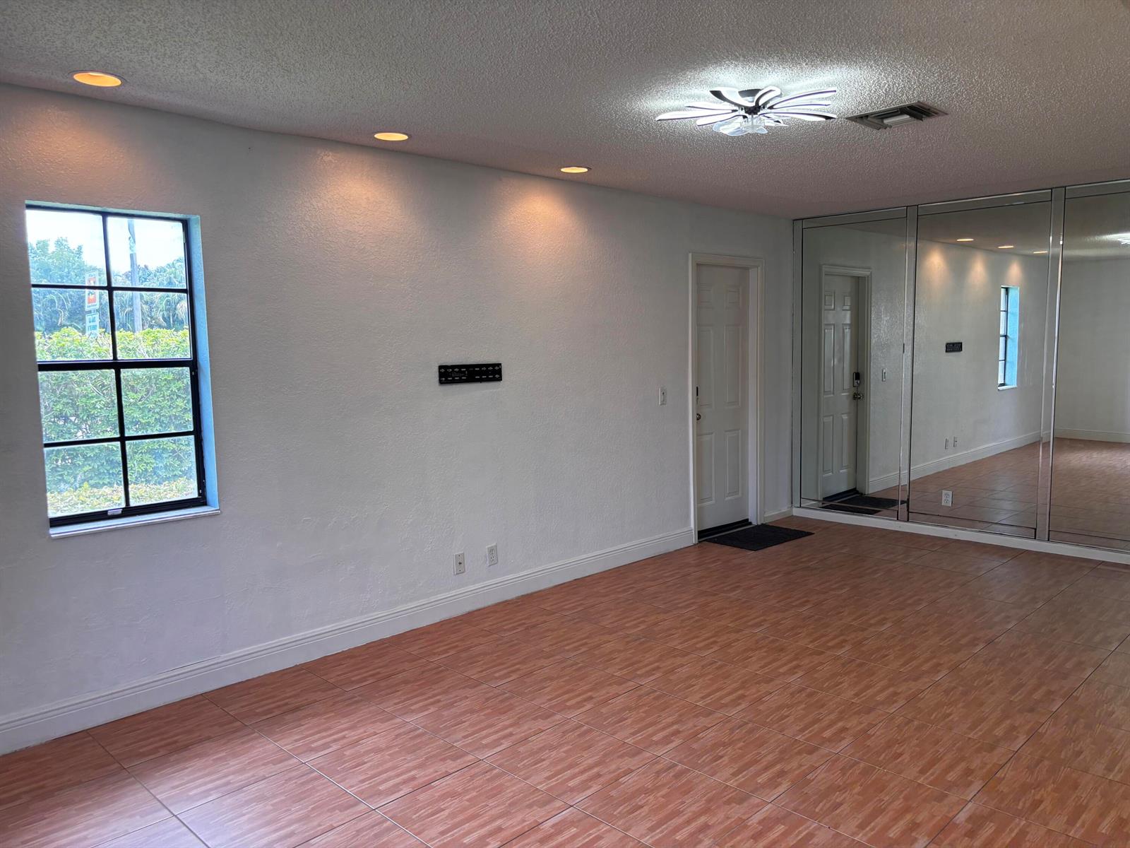 A room with white walls, tiled flooring, a window, a door, and mirrored closet doors — 12761 Westhampton Circle, Wellington FL 33414, WELLINGTON, FL