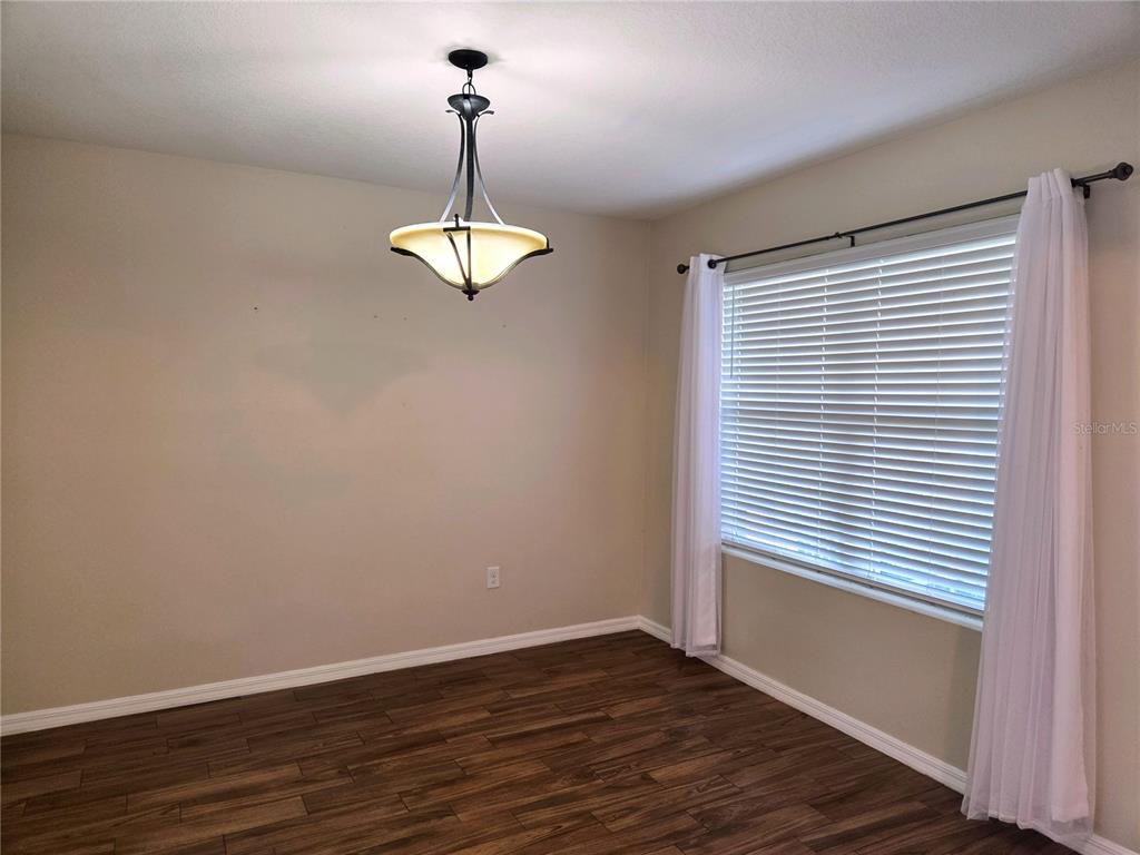 A dining room features dark wood-look flooring, a pendant light, and a window with blinds — 109 TIERRA VERDE WAY, BRADENTON, FL