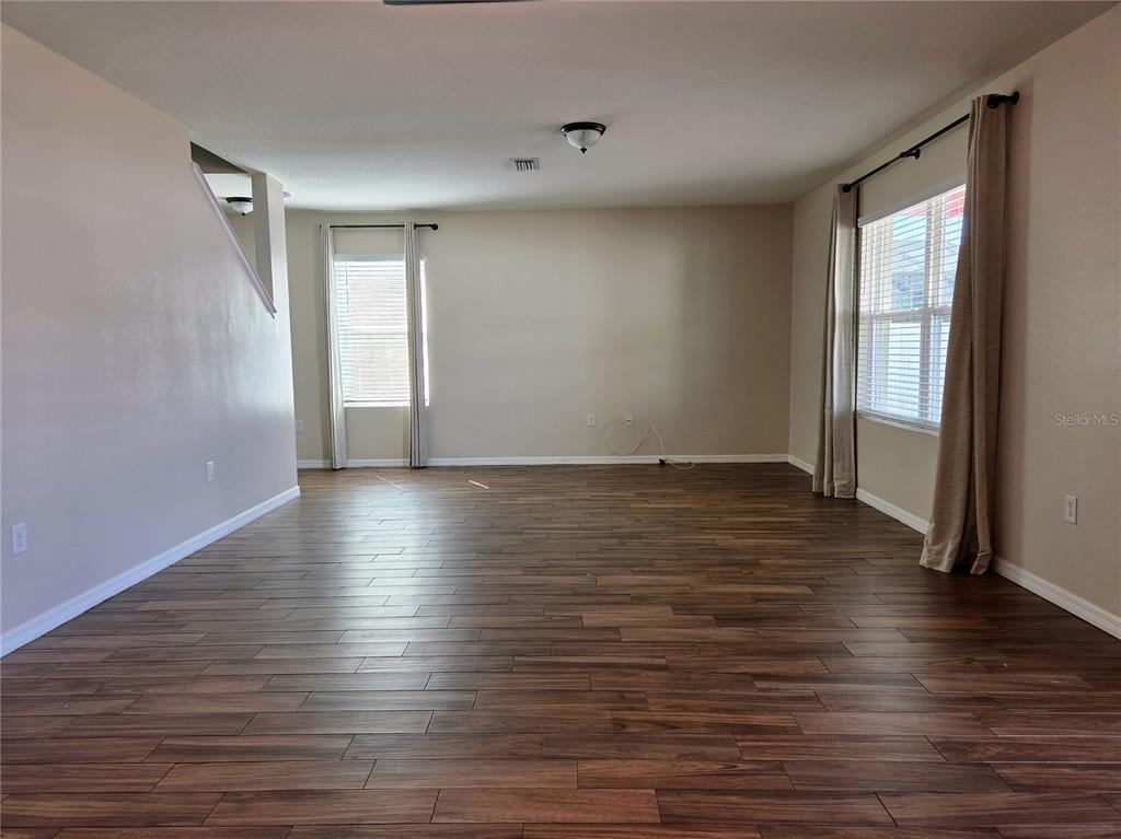 An empty living room features wood-look flooring, beige walls, and two windows with curtains — 109 TIERRA VERDE WAY, BRADENTON, FL