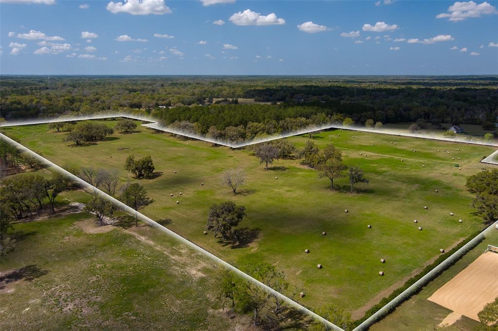 An aerial view shows a large, fenced grassy pasture dotted with trees and hay bales — 1100 SW 110TH AVENUE, OCALA, FL