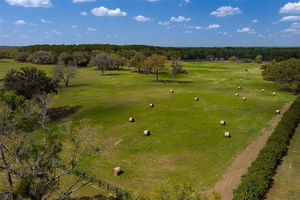 An aerial view of a large, grassy pasture dotted with hay bales and scattered trees — 1100 SW 110TH AVENUE, OCALA, FL