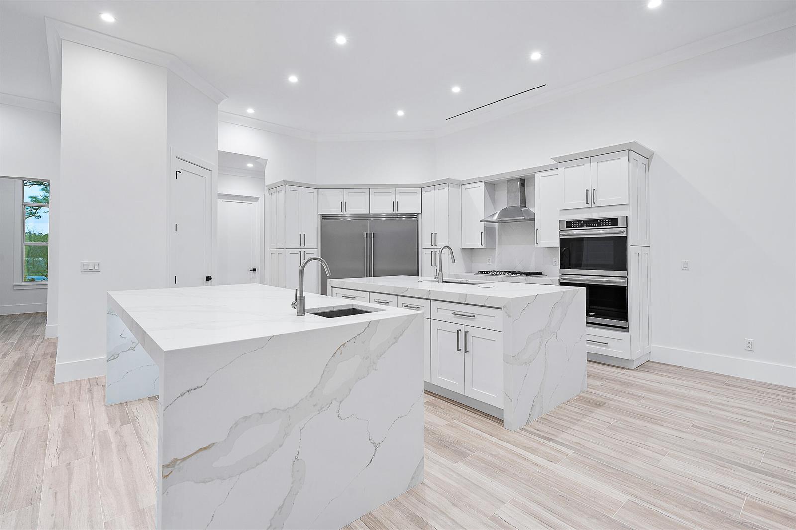 A modern white kitchen features two marble-topped islands, stainless steel appliances, and light wood flooring — 18211 SE Old Trail Drive W, Jupiter FL 33478, JUPITER, FL