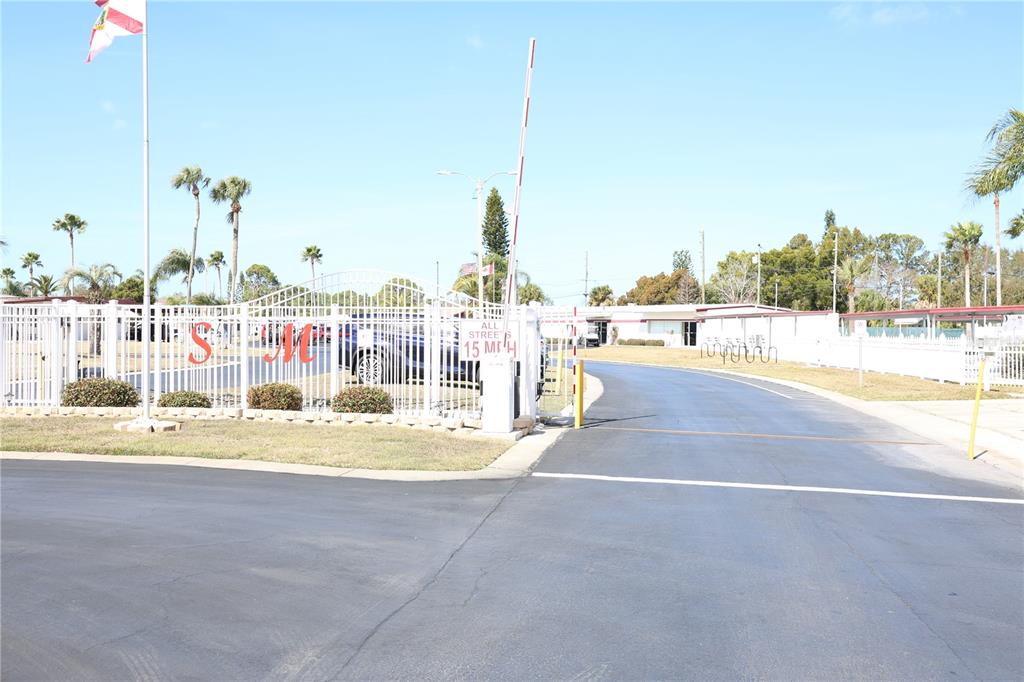 A gated entrance with a white fence and a raised barrier arm leads to a road — 6608 ROOSEVELT DRIVE, PORT RICHEY, FL