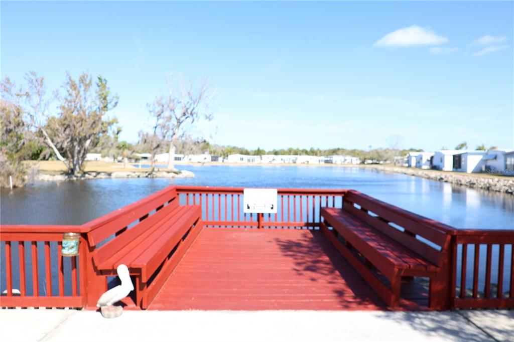 A red wooden deck with built-in benches overlooks a lake with houses in the distance — 6608 ROOSEVELT DRIVE, PORT RICHEY, FL