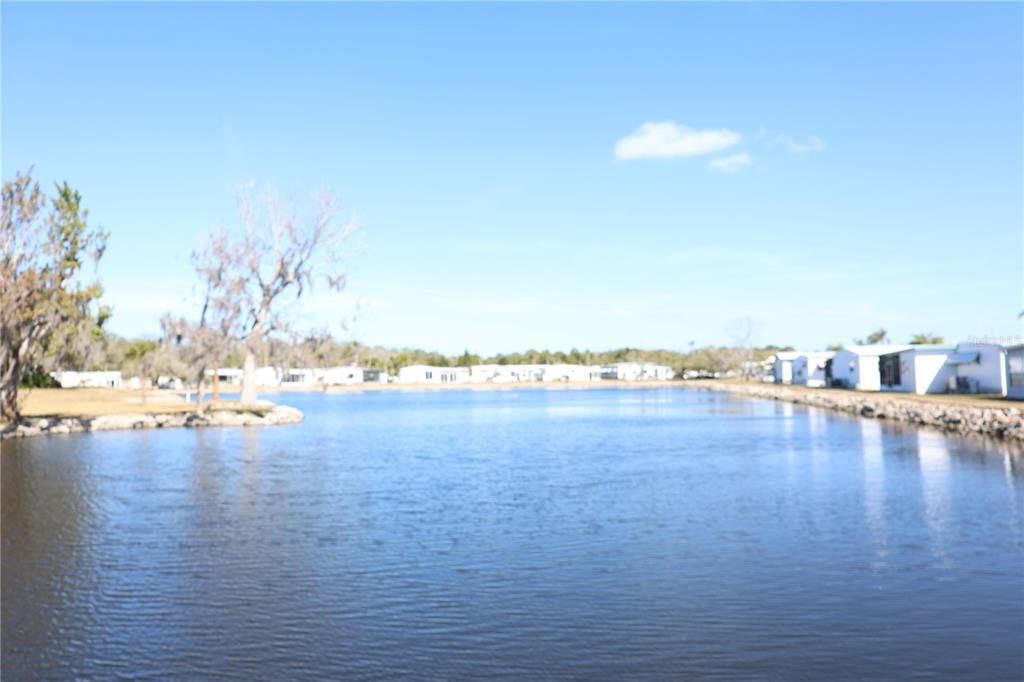 A view of a lake with mobile homes along the shoreline under a blue sky — 6608 ROOSEVELT DRIVE, PORT RICHEY, FL