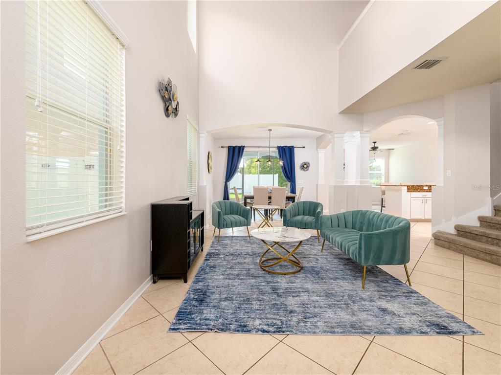 A living room with high ceilings, tile floors, a blue rug, and teal furniture — 12833 GENEVA GLADE DRIVE, RIVERVIEW, FL