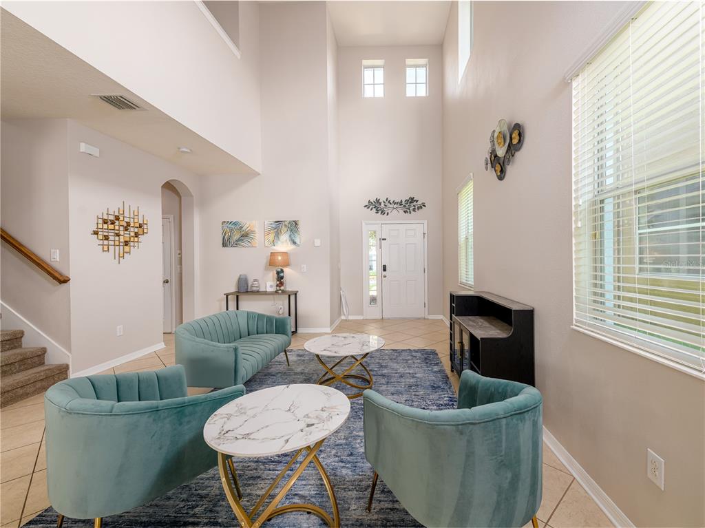 A high-ceilinged living room features teal velvet seating, marble-topped tables, and a blue area rug — 12833 GENEVA GLADE DRIVE, RIVERVIEW, FL