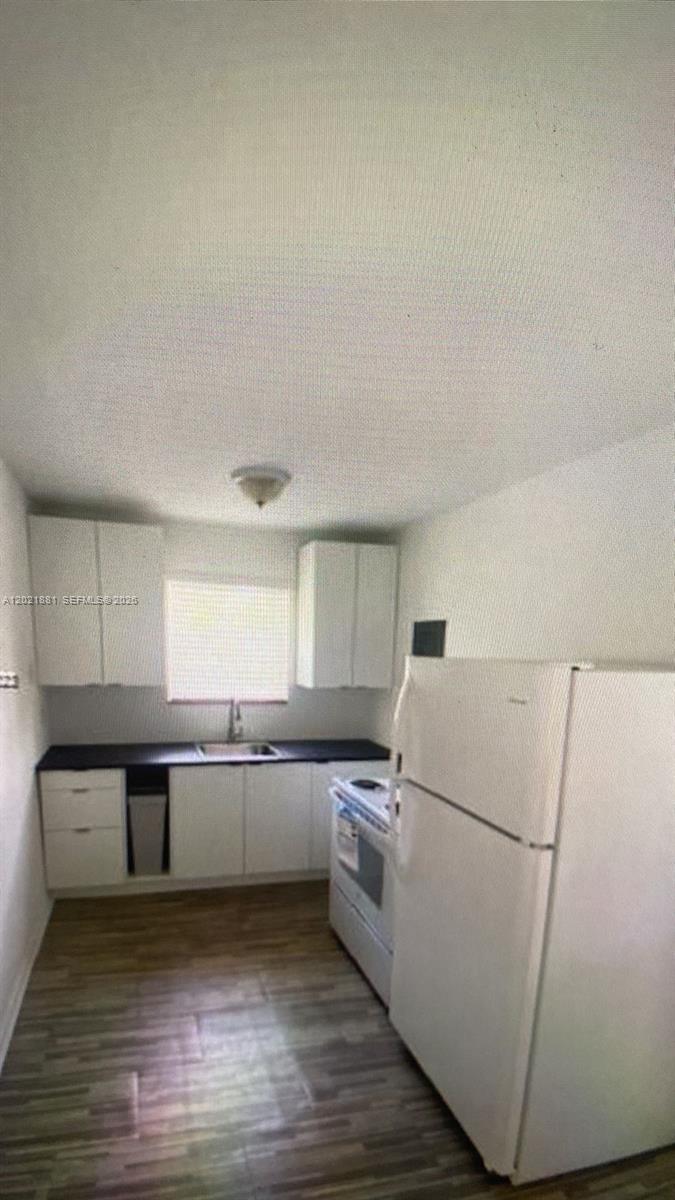 A small kitchen features white cabinets, dark countertops, a white refrigerator, and wood-look flooring — 7637 NW 3rd Ave, Miami FL 33150, MIAMI, FL