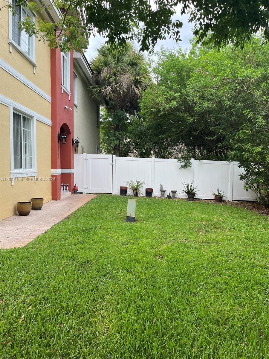 A grassy backyard features a paved walkway, a white vinyl fence, and potted plants — 5347 SW 40th Ave # 5347, Dania Beach FL 33314, DANIA BEACH, FL