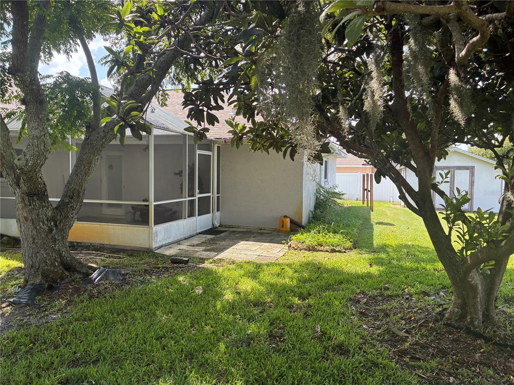 A grassy backyard features several large trees and shrubs next to a white house — 176 BREN MAR LANE, PALM COAST, FL