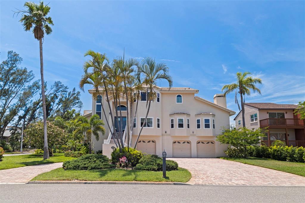 A three-story beige house with a three-car garage and palm trees in the front yard — 1156 2ND AVENUE S, TIERRA VERDE, FL