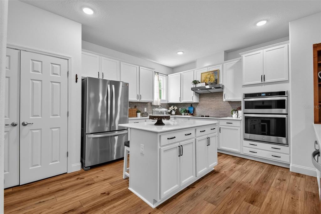 A white kitchen features a central island, stainless steel appliances, and wood-look flooring — 48 OAKLEAF WAY, PALM COAST, FL