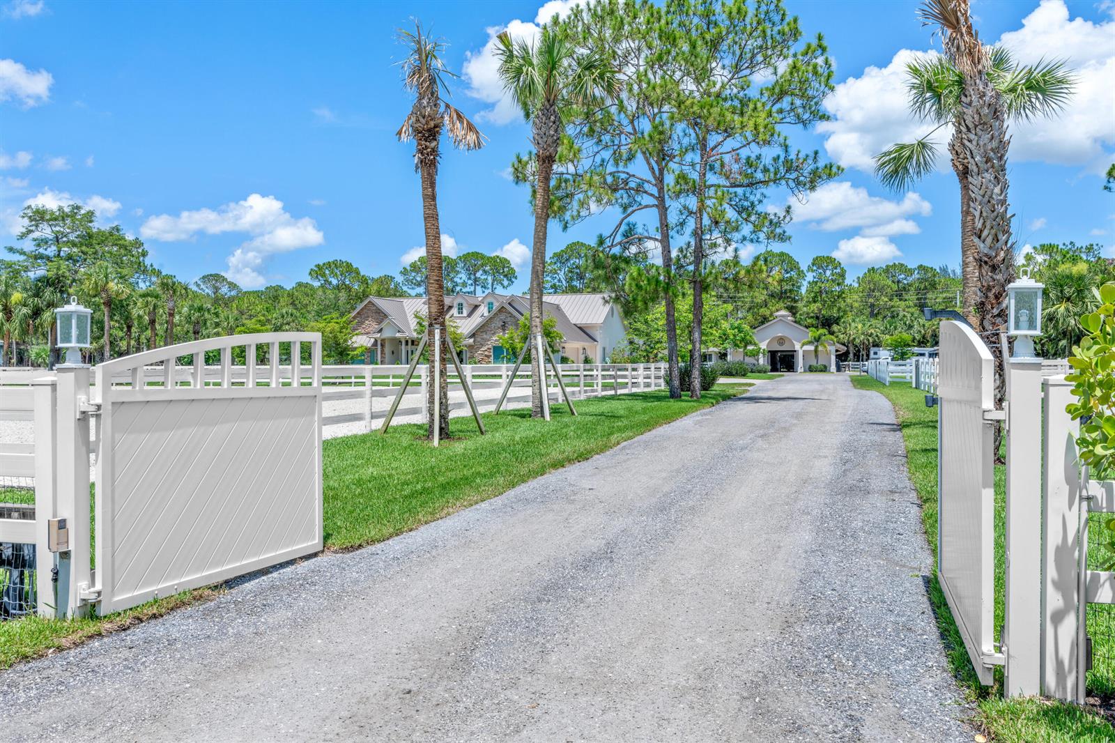 A gravel driveway leads through an open white gate toward a house and outbuilding — 1464 Stallion Drive, Loxahatchee FL 33470, LOXAHATCHEE, FL