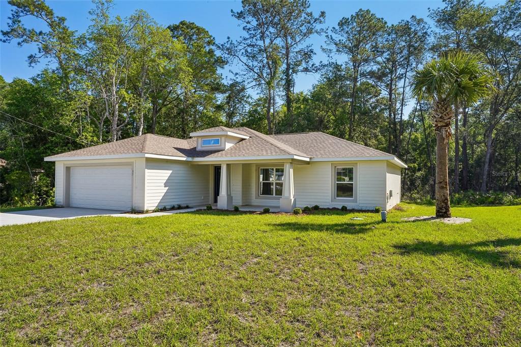 A single-story house with light siding, a two-car garage, and a palm tree in front — 8973 N TROJAN DRIVE, CITRUS SPRINGS, FL