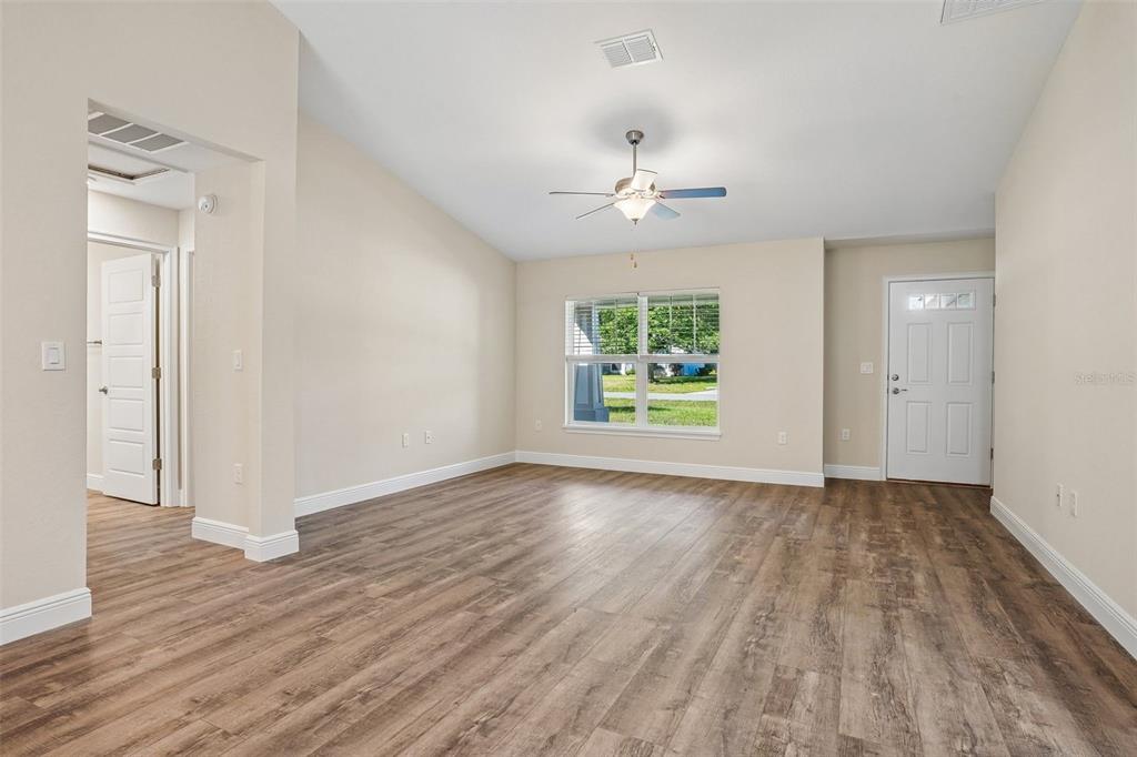 An empty living room features wood-look flooring, a ceiling fan, and a front entry door — 8973 N TROJAN DRIVE, CITRUS SPRINGS, FL