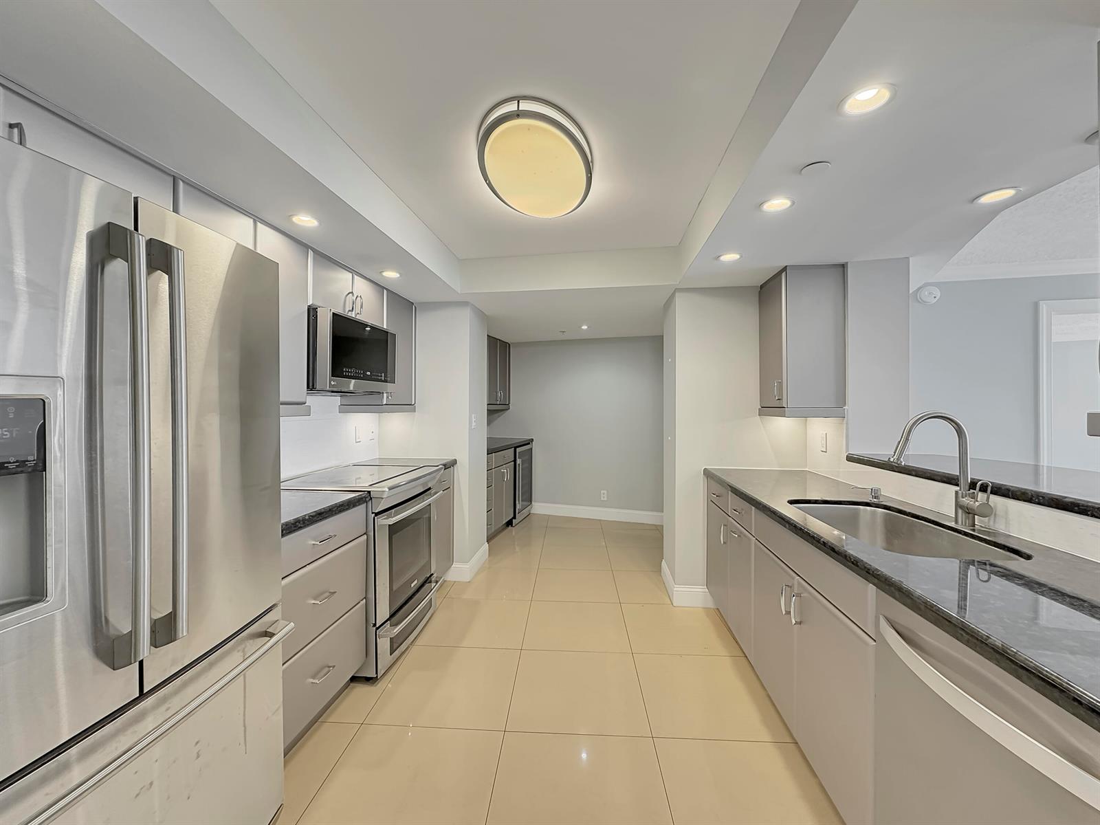 A galley kitchen features stainless steel appliances, grey cabinetry, dark countertops, and light tile flooring — 3000 N Ocean Drive, Singer Island FL 33404, SINGER ISLAND, FL