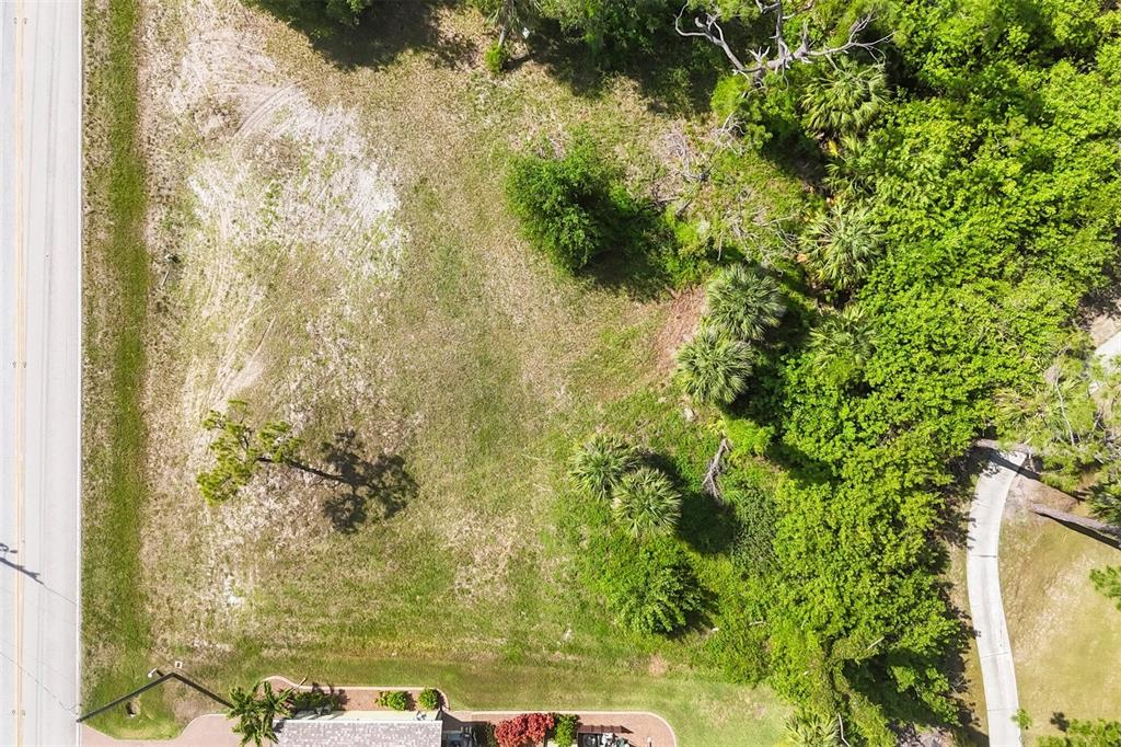 An aerial view shows a vacant, grassy residential lot bordered by a road and trees — 760 ROTONDA CIRCLE, ROTONDA WEST, FL