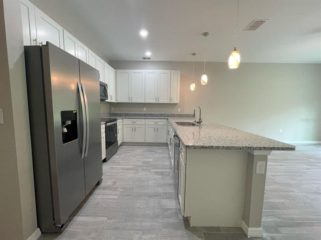 A kitchen features white cabinets, granite countertops, stainless steel appliances, and gray tile flooring — 407 BEDLINGTON COURT, KISSIMMEE, FL