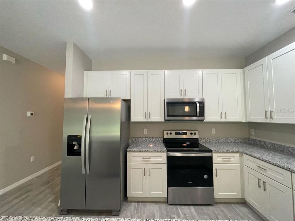 A kitchen features white cabinets, stainless steel appliances, and speckled granite countertops — 407 BEDLINGTON COURT, KISSIMMEE, FL
