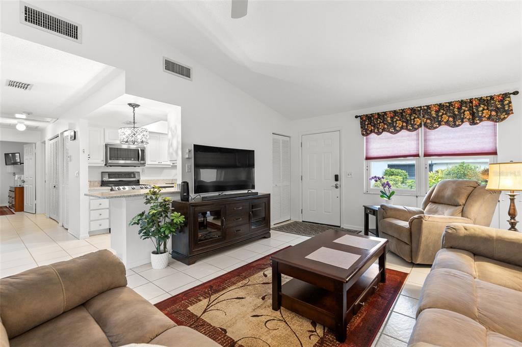 A living room with tile floors, a television console, and an open kitchen area — 3143 37TH LANE S UNIT B, ST PETERSBURG, FL