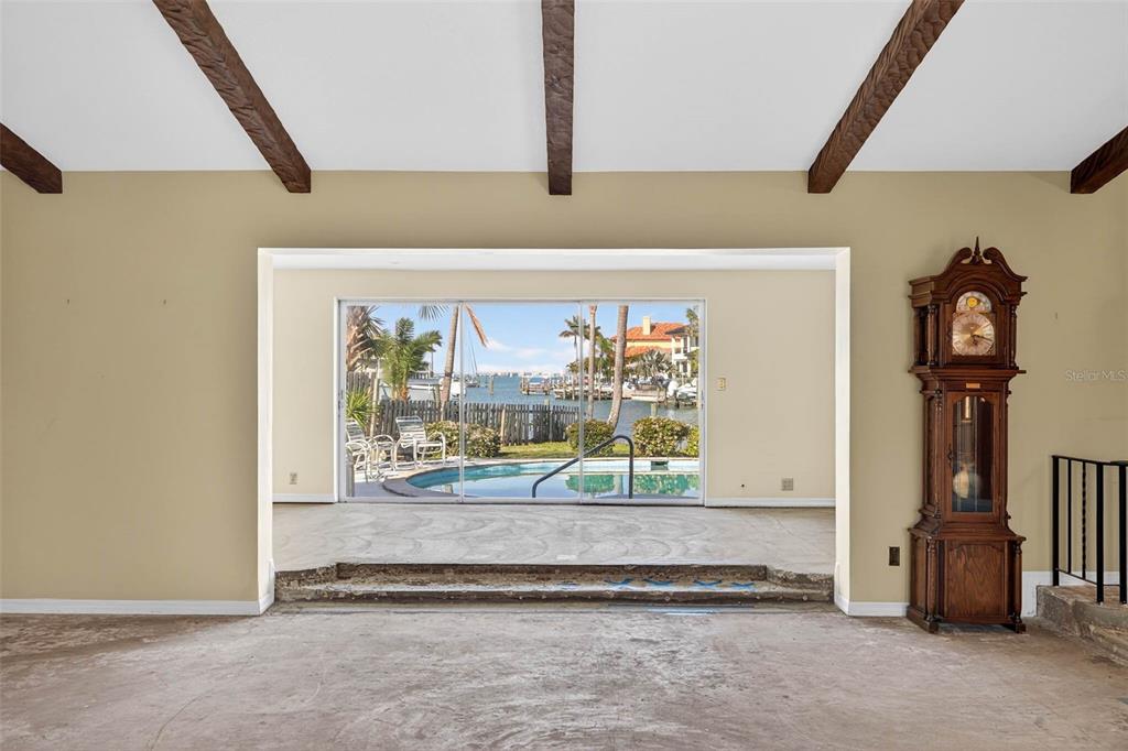 A living room with exposed ceiling beams, a grandfather clock, and a step-down pool view — 3103 WEDGEWOOD DRIVE, BELLEAIR BEACH, FL