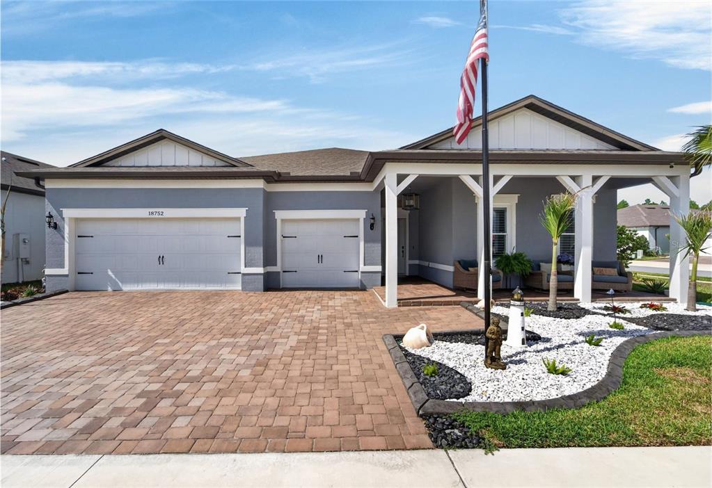 A gray single-story house features a paver driveway, a covered front porch, and white trim — 18752 HORIZON VIEW POINT, LAND O LAKES, FL