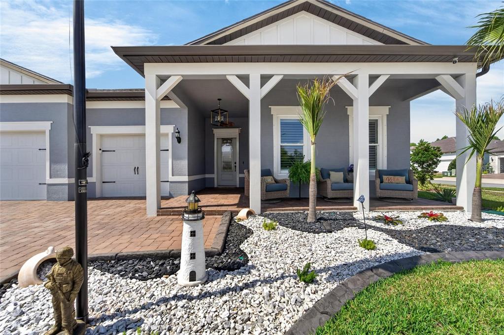 The exterior of a gray house features a covered porch, a lighthouse statue, and landscaping — 18752 HORIZON VIEW POINT, LAND O LAKES, FL
