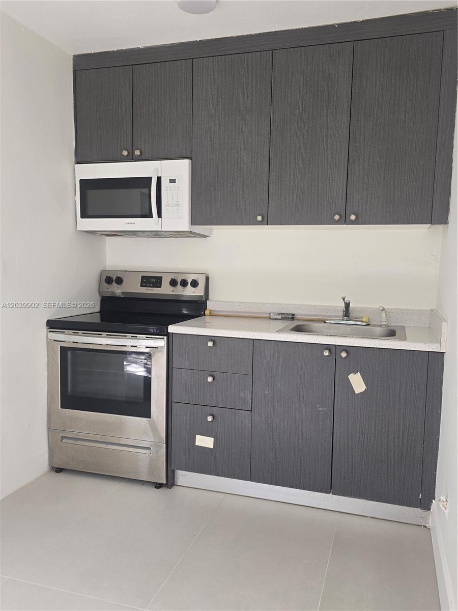 A small kitchen features dark wood-grain cabinets, stainless steel appliances, and a light countertop — 237 SW 13th St # 4, Dania Beach FL 33004, DANIA BEACH, FL