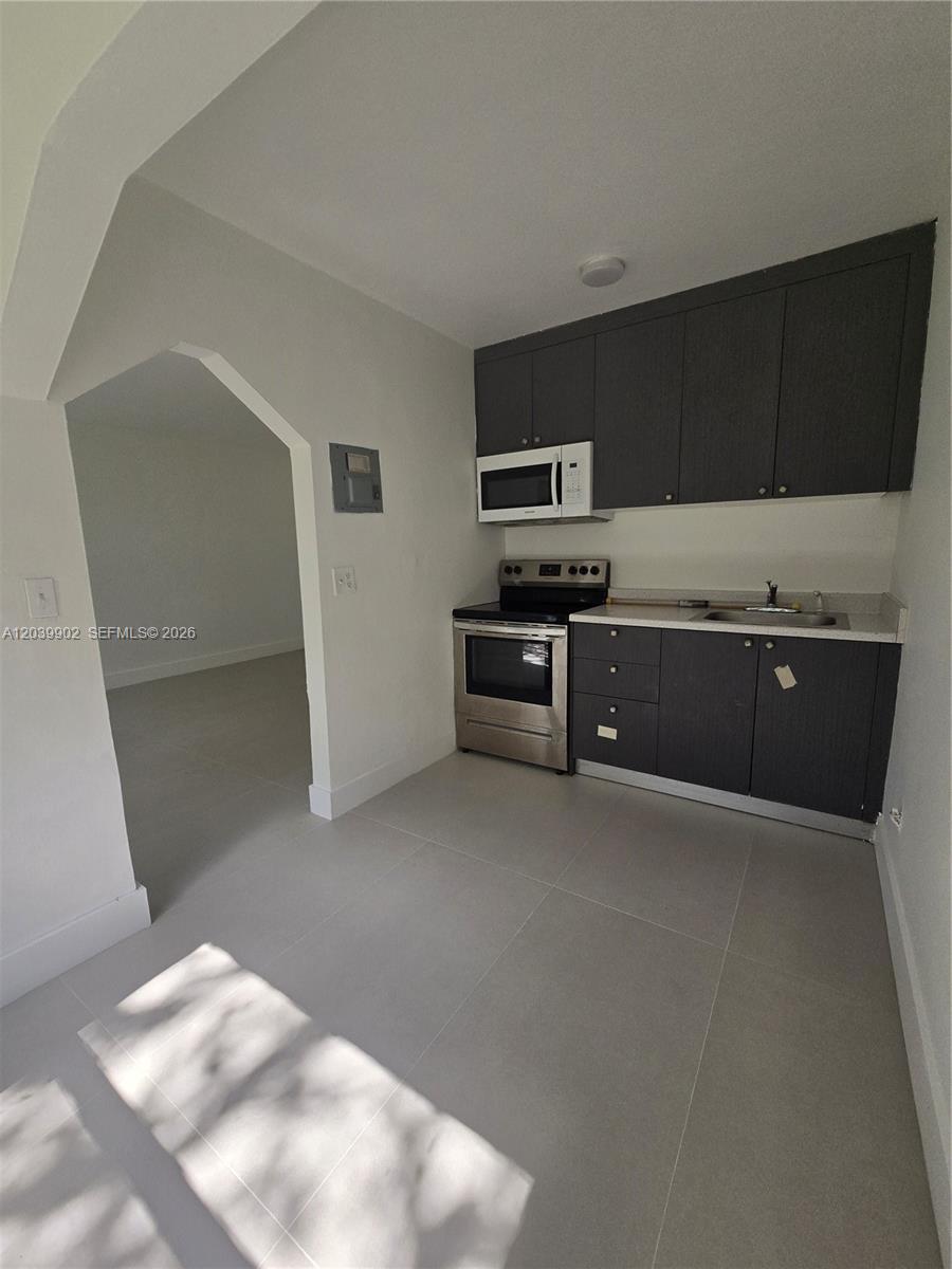 A small kitchen features dark gray cabinets, stainless steel appliances, and light gray floor tiles — 237 SW 13th St # 4, Dania Beach FL 33004, DANIA BEACH, FL