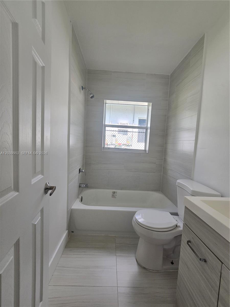 A bathroom features a white bathtub, a toilet, a vanity, and light-colored tile walls — 237 SW 13th St # 4, Dania Beach FL 33004, DANIA BEACH, FL
