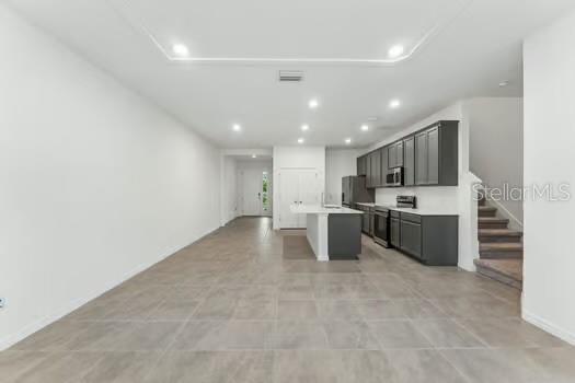 An open-concept kitchen and living area features gray cabinetry, a central island, and tile flooring — 7043 TWILIGHT BAY DRIVE, WINTER GARDEN, FL