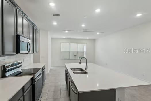 A modern kitchen features dark gray cabinets, a white quartz island, and stainless steel appliances — 7043 TWILIGHT BAY DRIVE, WINTER GARDEN, FL
