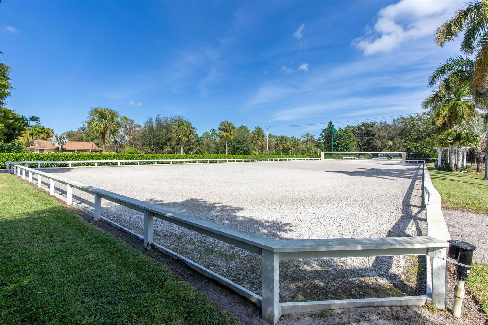 A large, fenced-in equestrian riding arena with a gravel surface sits under a blue sky — 14943 Paddock Drive, Wellington FL 33414, WELLINGTON, FL